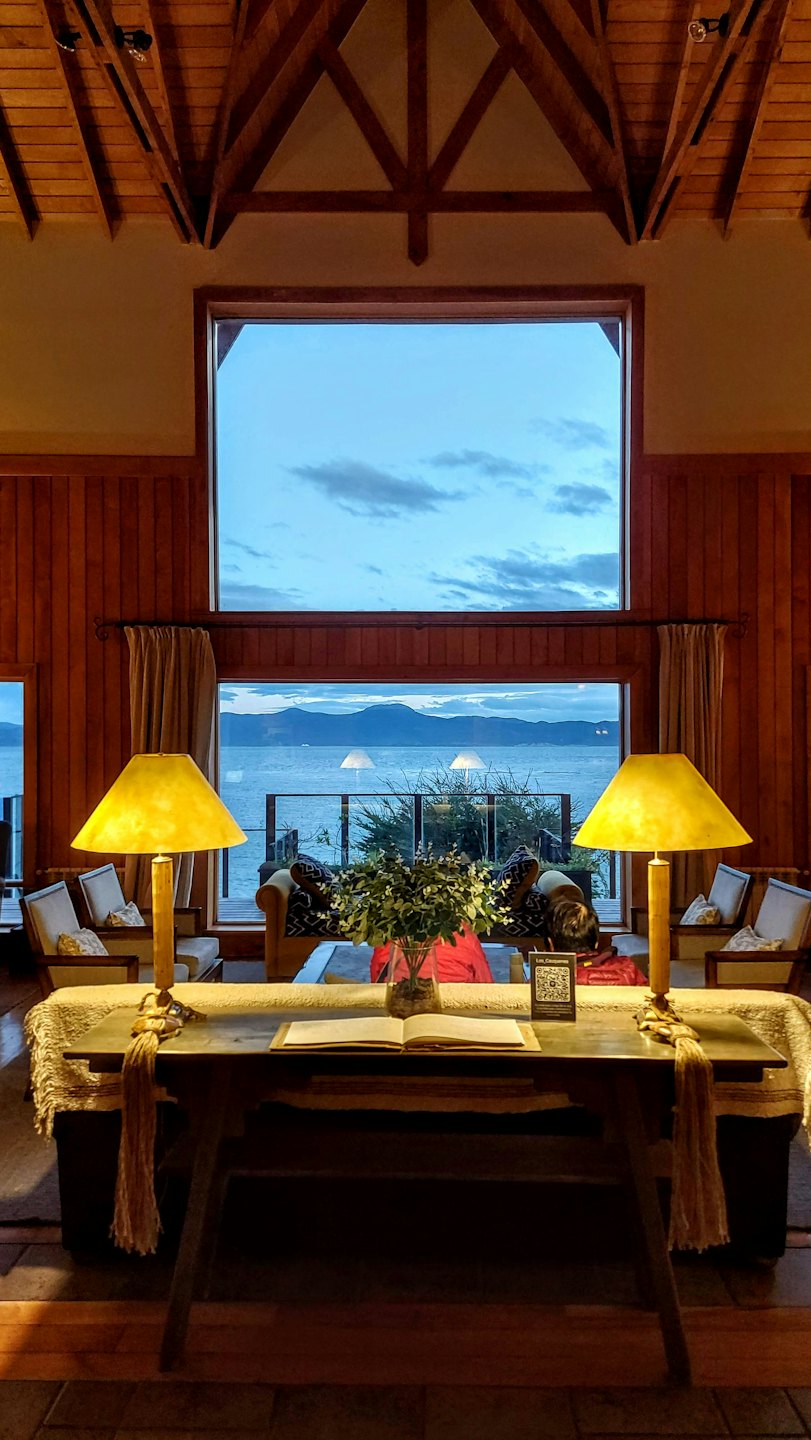 Cozy lodge interior with table set by a large window overlooking a lake.