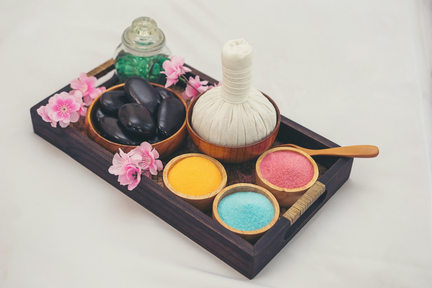 Massage stones and bath salts arranged on a wooden tray.